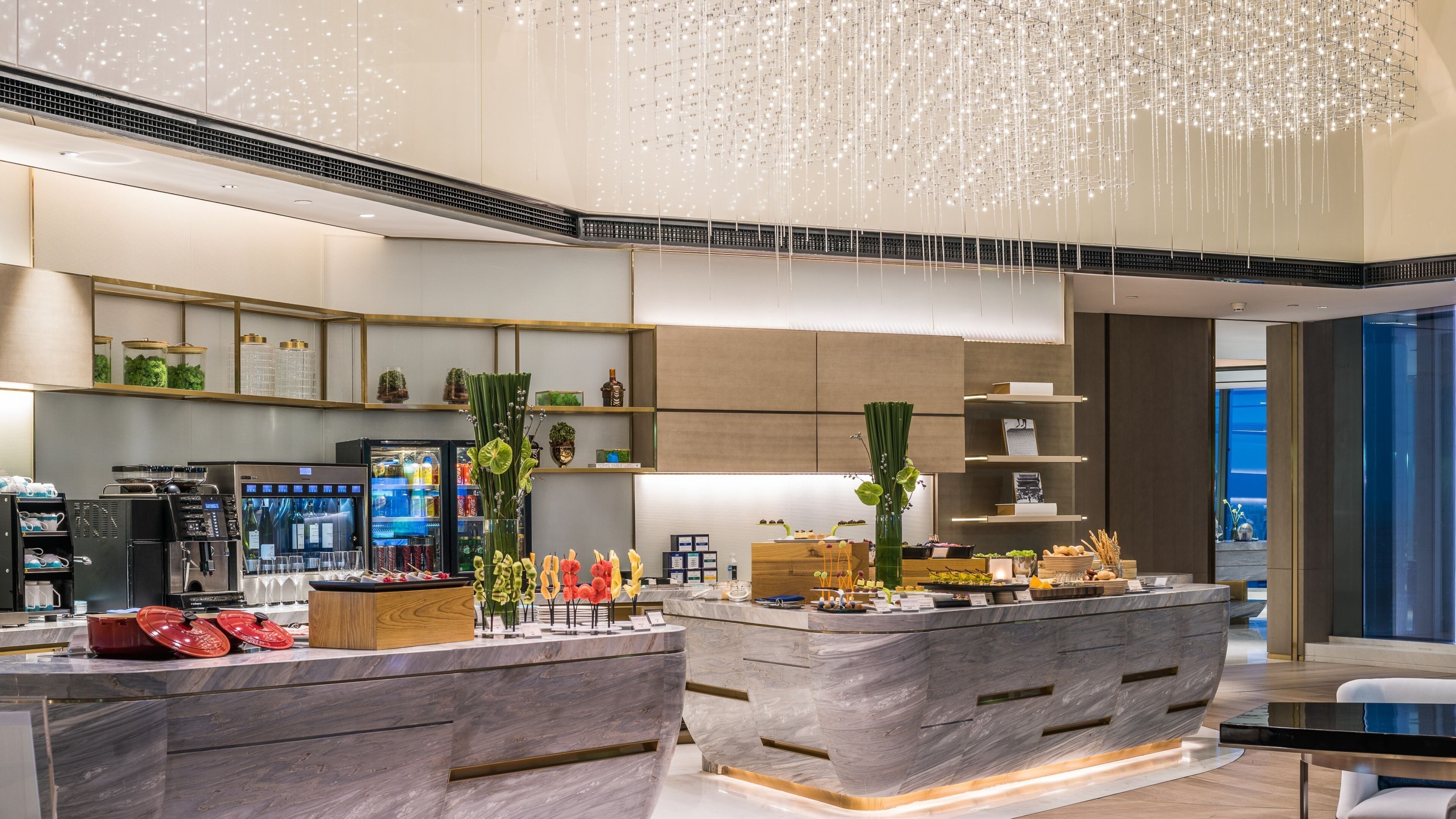 A modern kitchen with marble countertops, a central island, and a hanging light fixture.