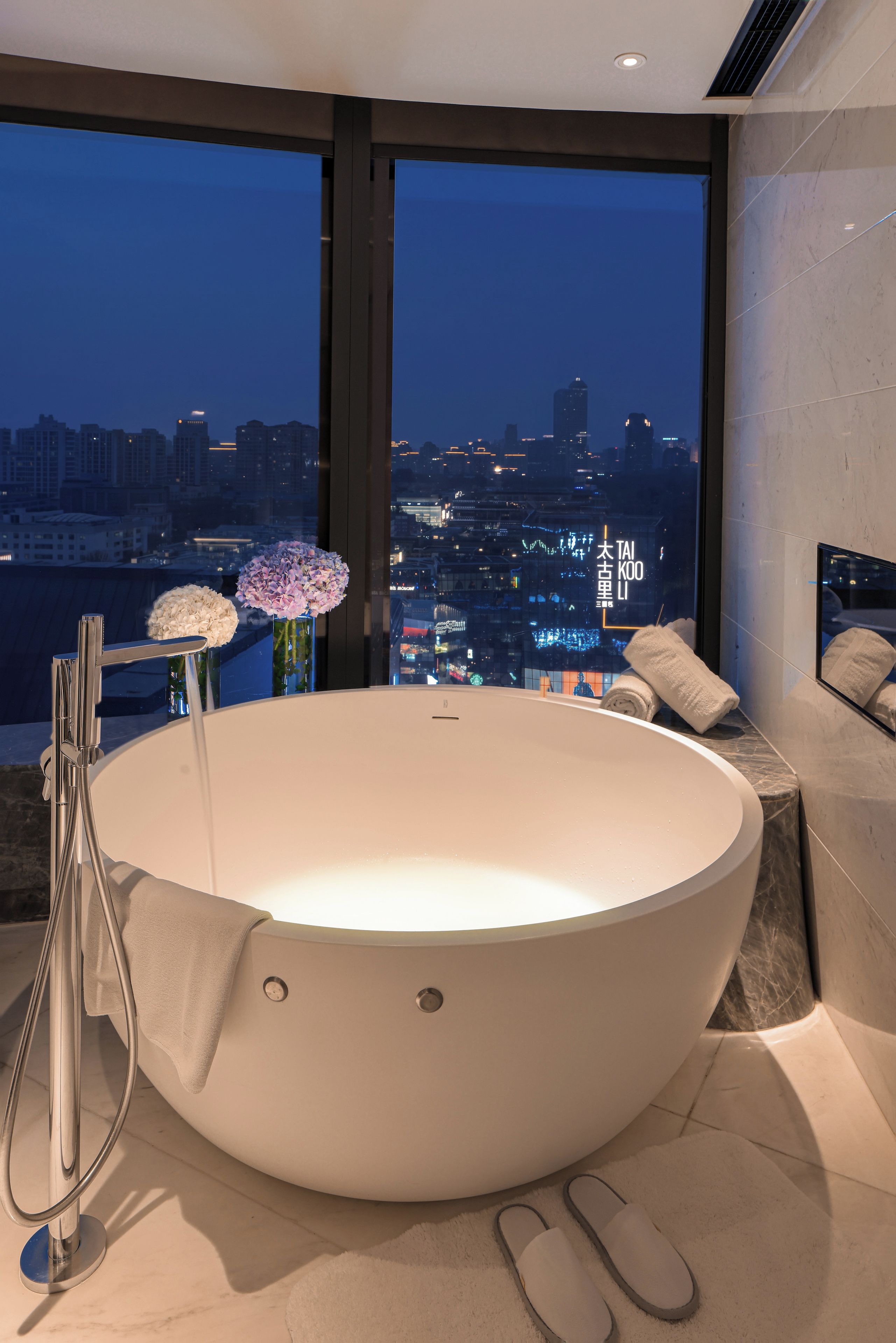 A modern bathroom with a large bathtub, a glass shower enclosure, and a city view.