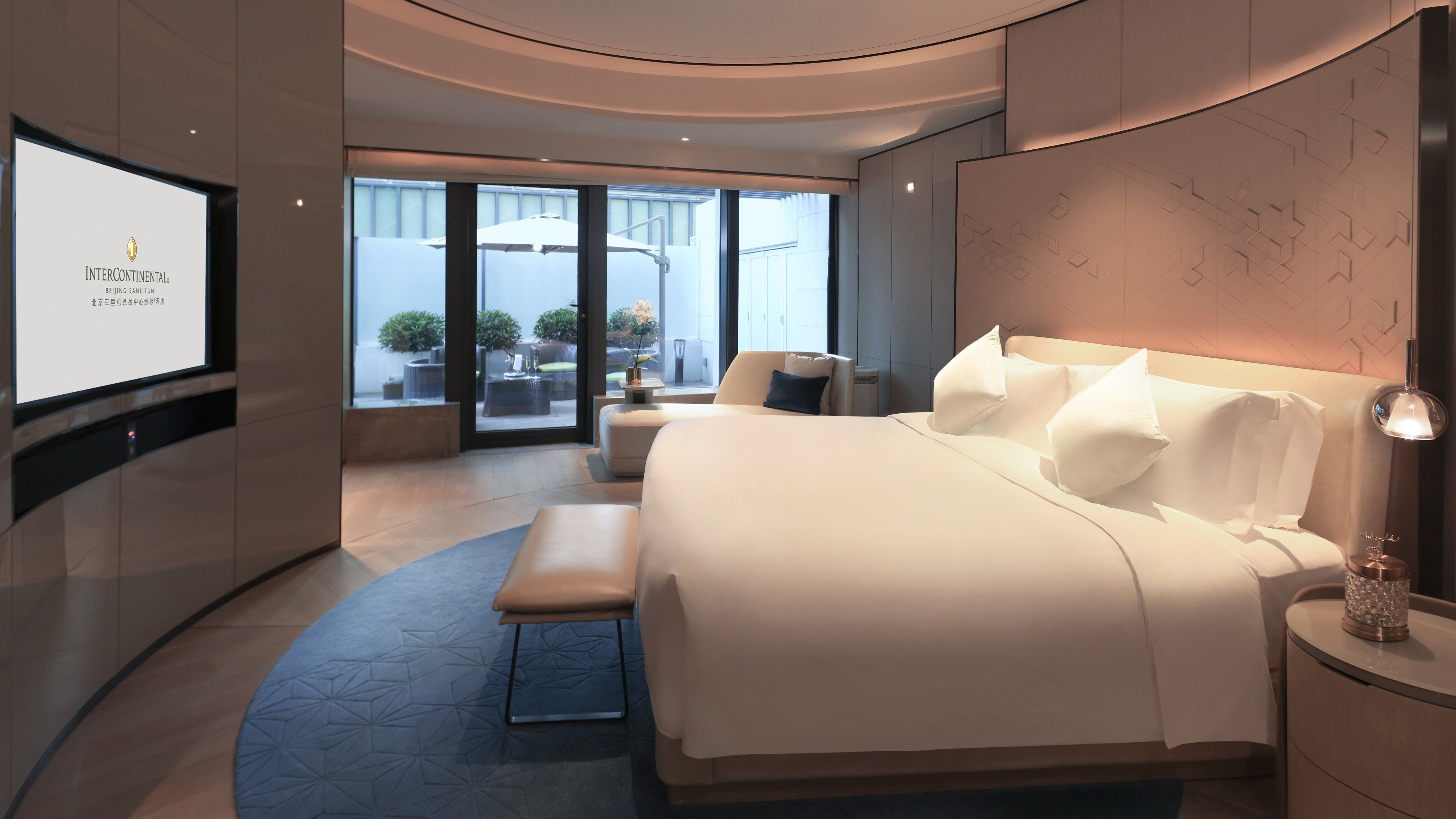 A modern hotel room with a large bed, a seating area, and a TV displaying 'InterContinental'.
