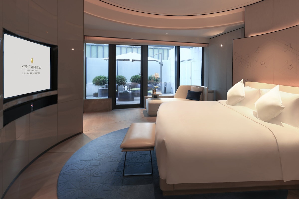 A modern hotel room with a large bed, a seating area, and a TV displaying 'InterContinental'.