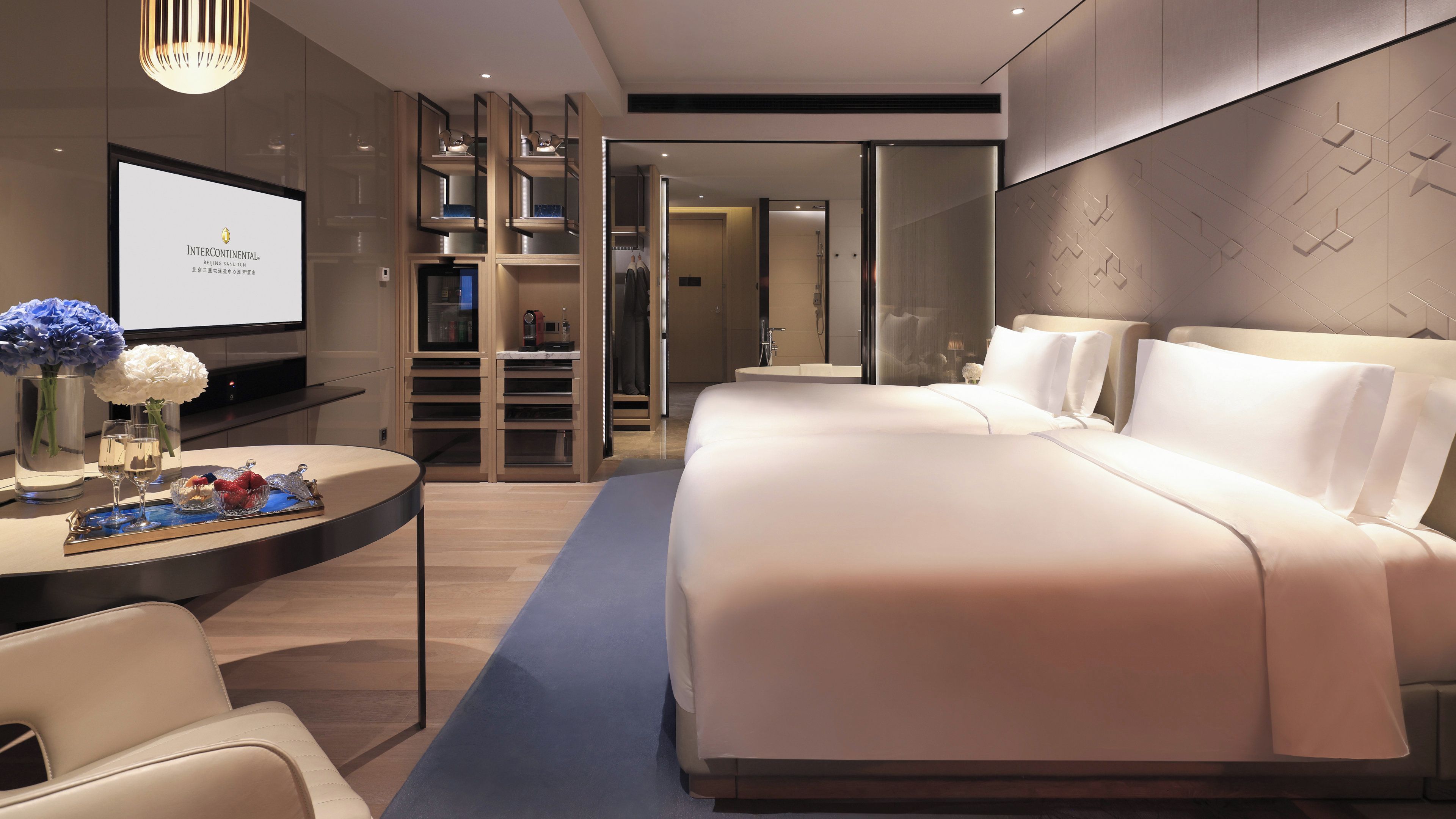A modern hotel room with a large bed, a desk with a laptop, and a television.