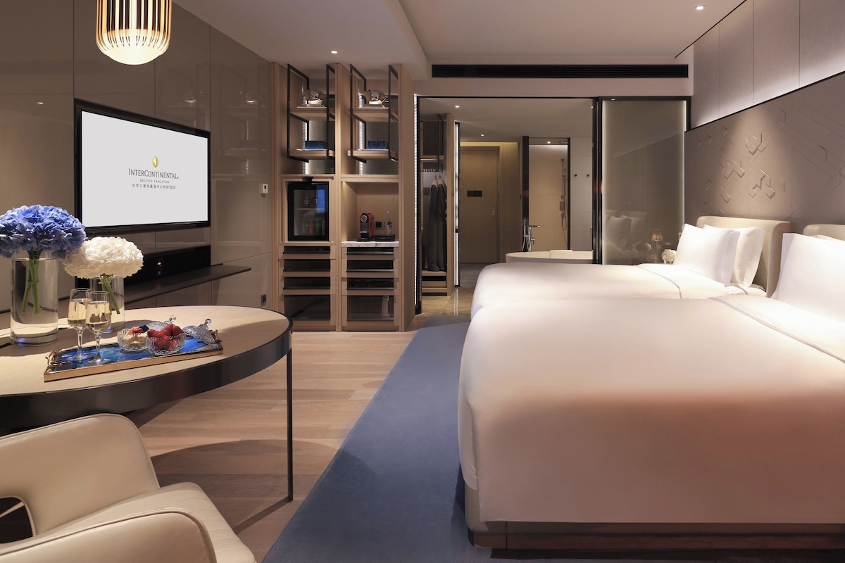 A modern hotel room with a large bed, a desk with a laptop, and a television.