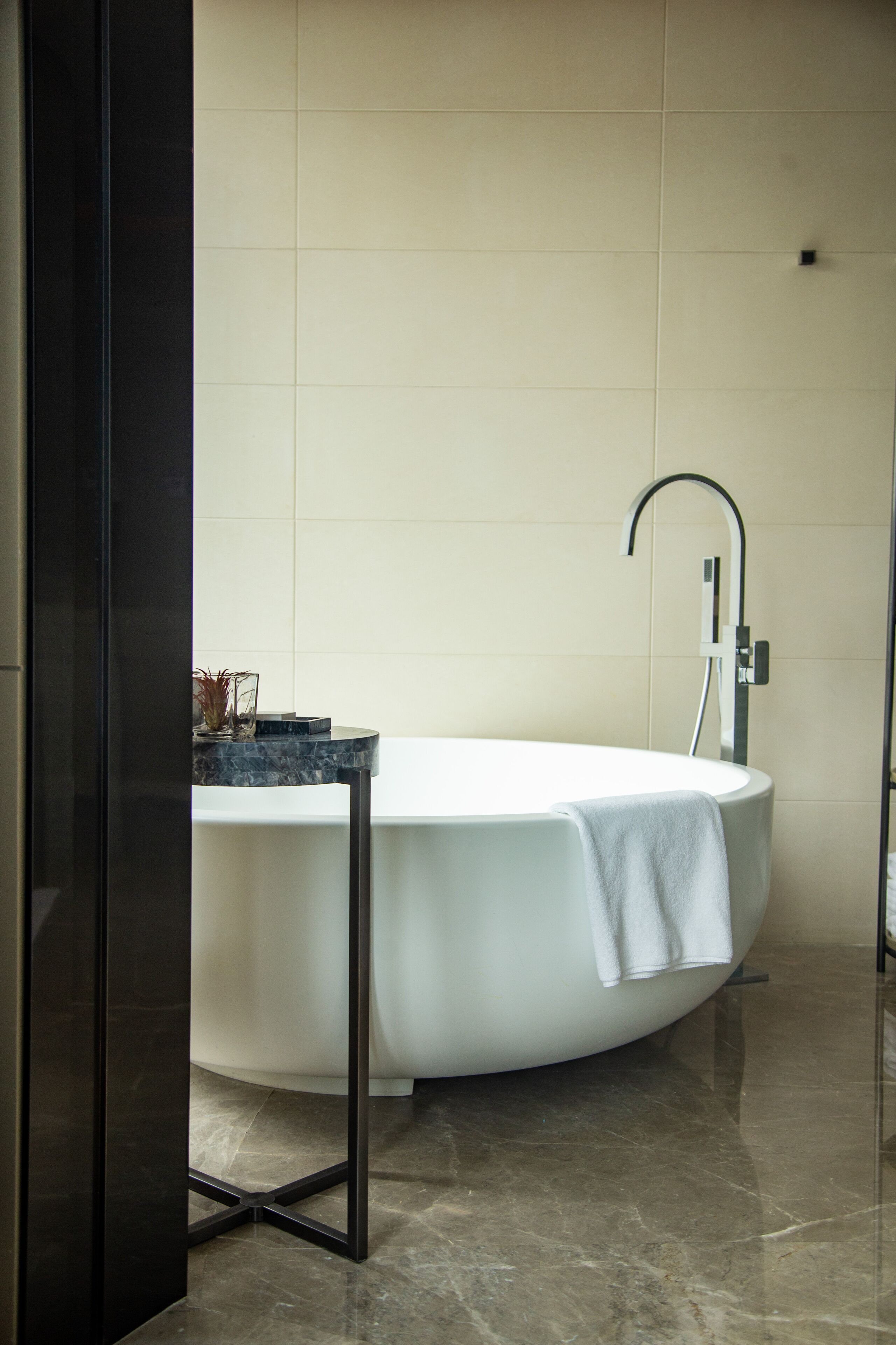 Un baño moderno con una bañera independiente, una mesita con un florero y una toalla sobre la bañera.