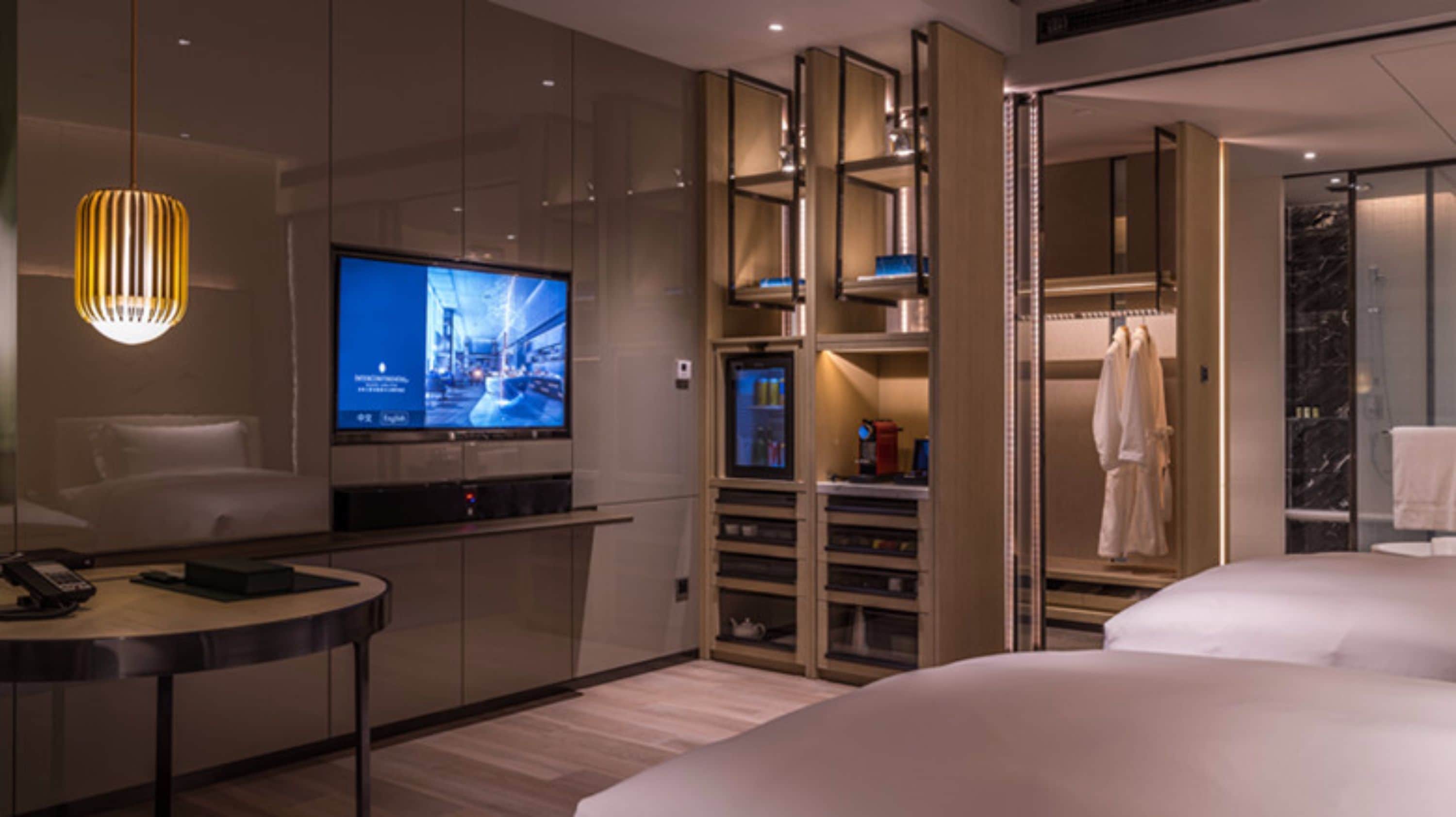 Een moderne hotelkamer met een grote flatscreen televisie, een nachtkastje met een telefoon, een kledingkast met inbouwplanken en een aparte badkamer met een marmeren douche.