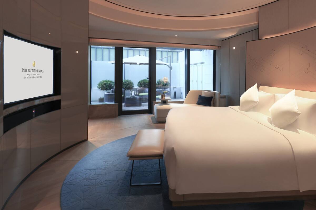 A modern hotel room with a large bed, a seating area, and a TV displaying 'InterContinental'.