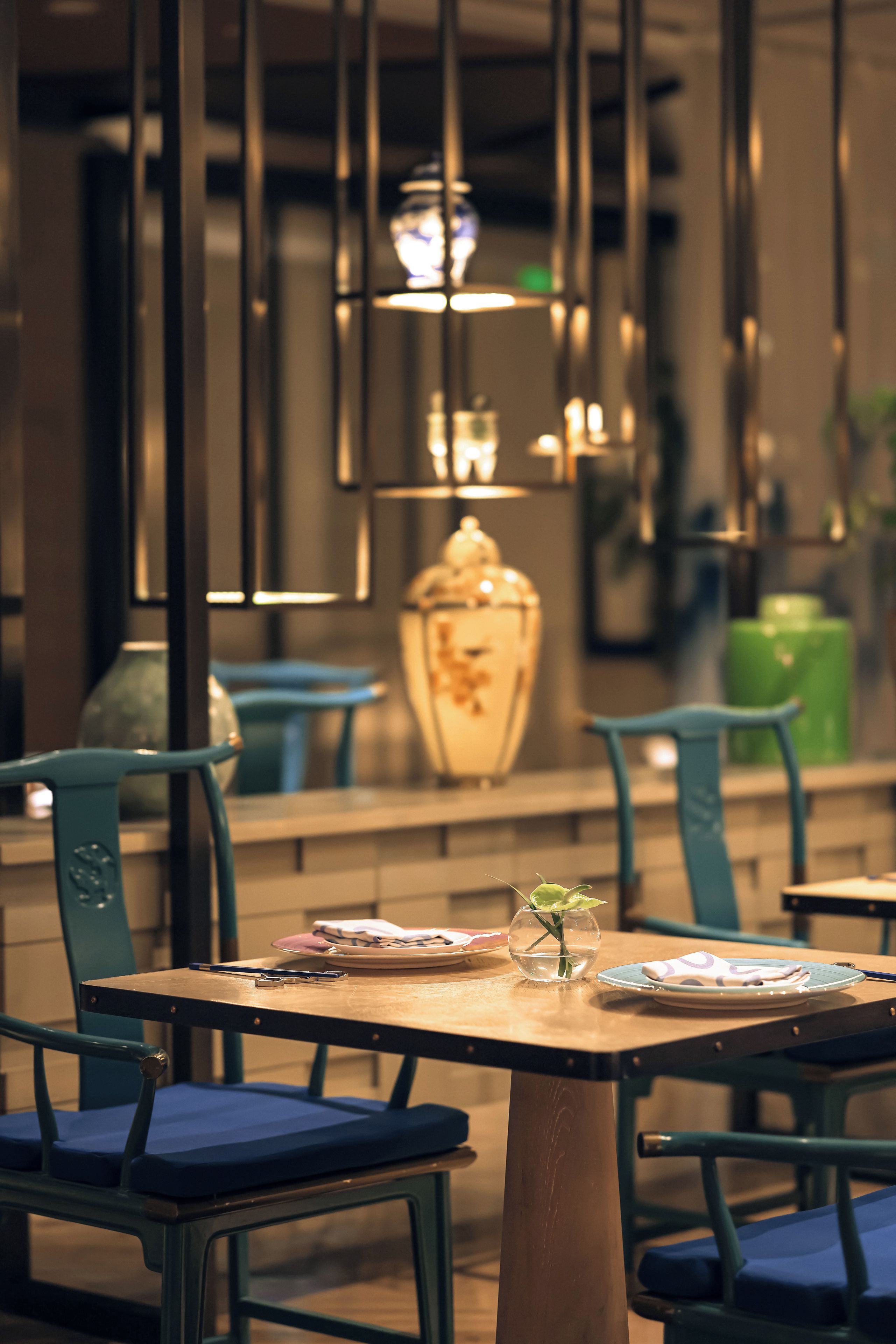 A dining area with tables and chairs, a vase with a plant, and hanging lights.
