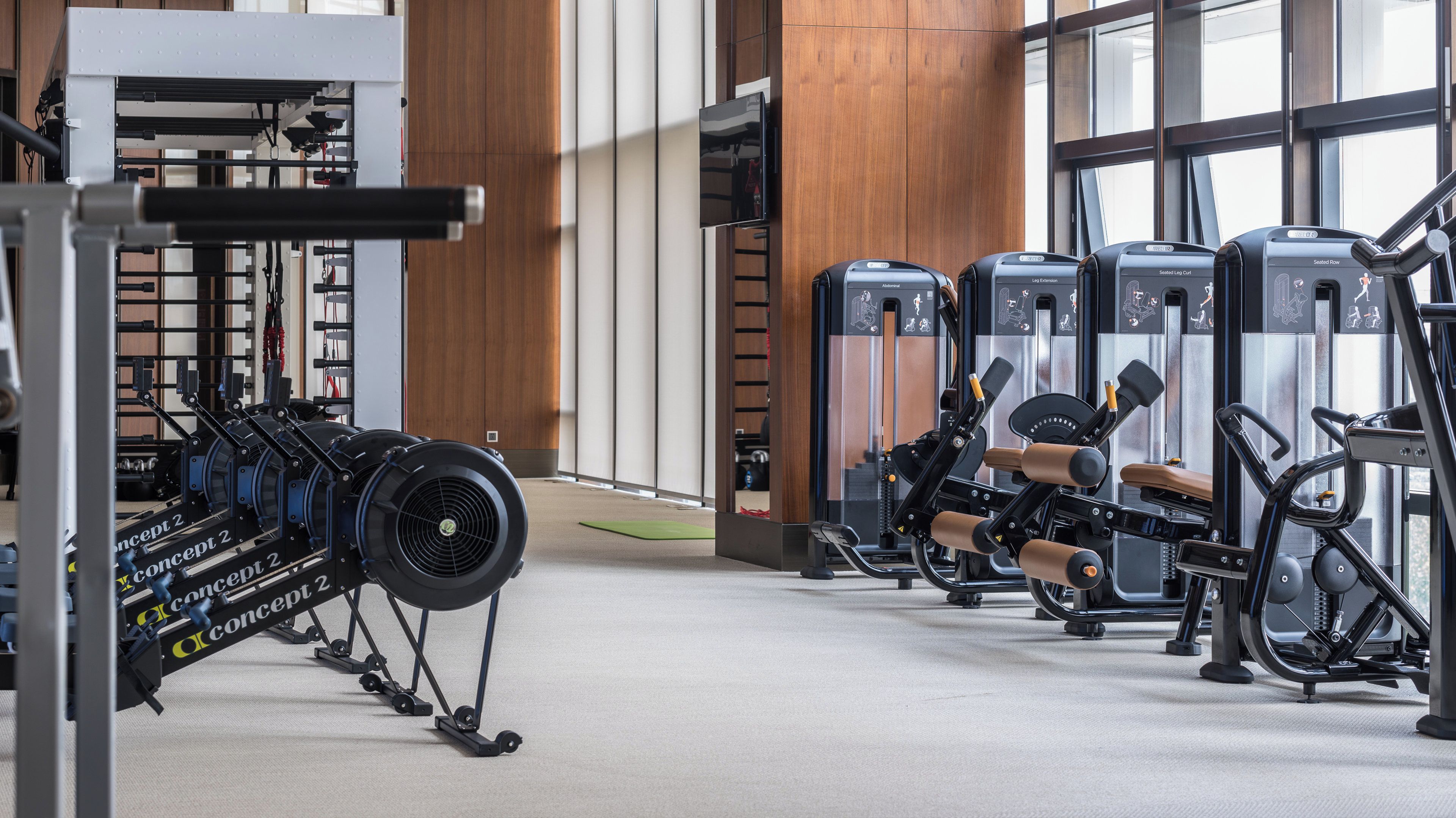 A gym with various exercise equipment, including a rowing machine, leg extension machine, and seated row machine.