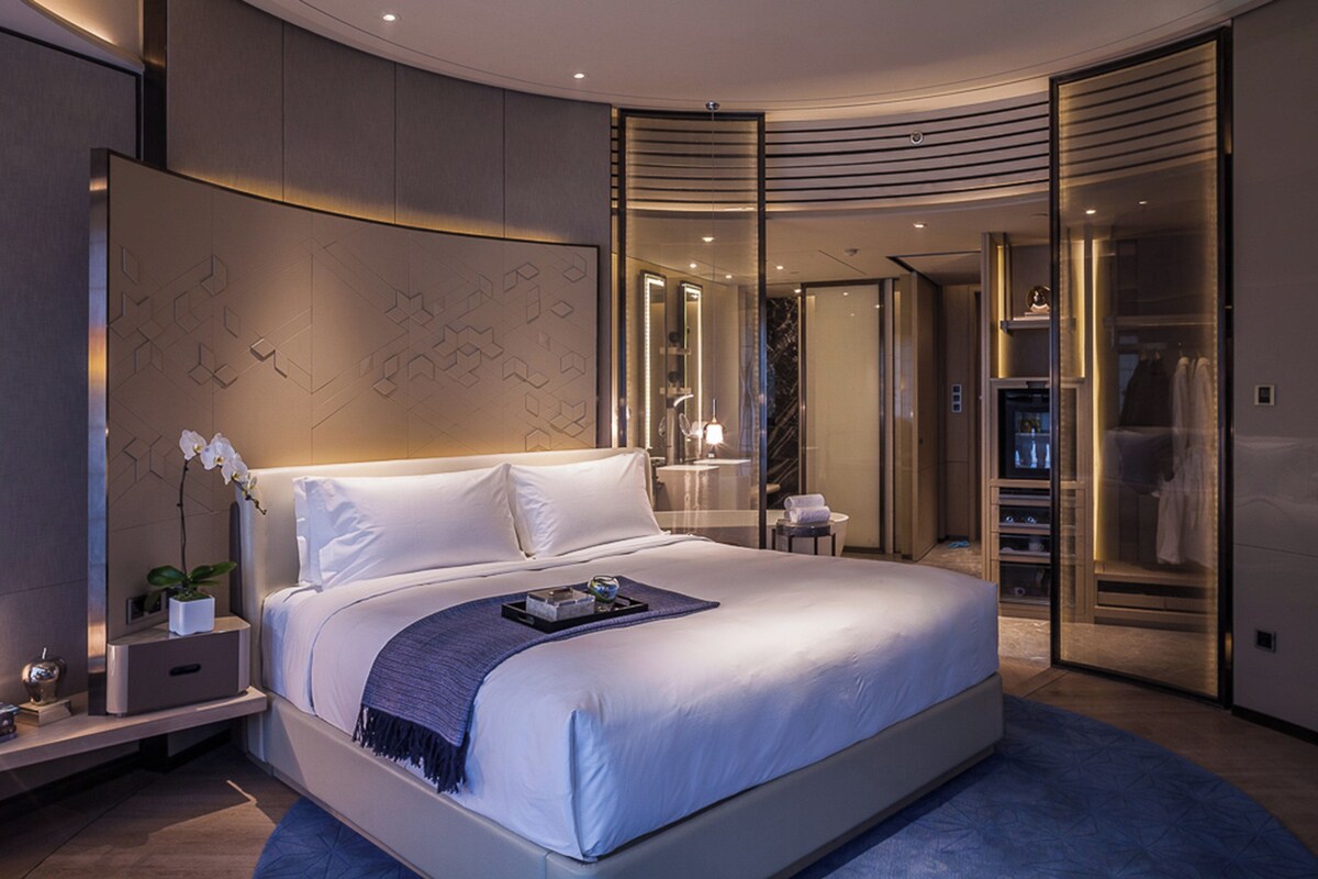 A modern bedroom with a large bed, a nightstand, a potted plant, and a walk-in closet.