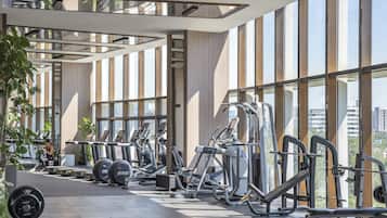Une salle de sport moderne, dotée de divers appareils d’entraînement, de grandes fenêtres et offrant une vue sur la ville.