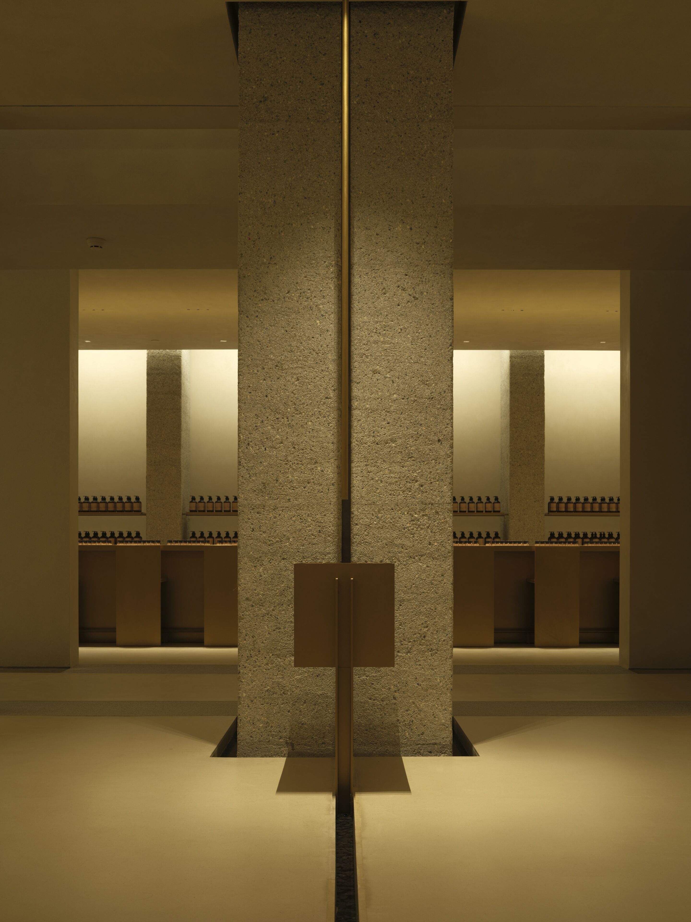 A modern interior with a central column, recessed lighting, and a symmetrical arrangement of shelves with bottles.