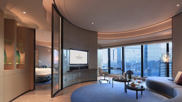 Una habitación de hotel moderna con techo curvo, un ventanal grande con vistas a la ciudad, un televisor de pantalla plana y una zona de estar con sofá y mesa de centro.