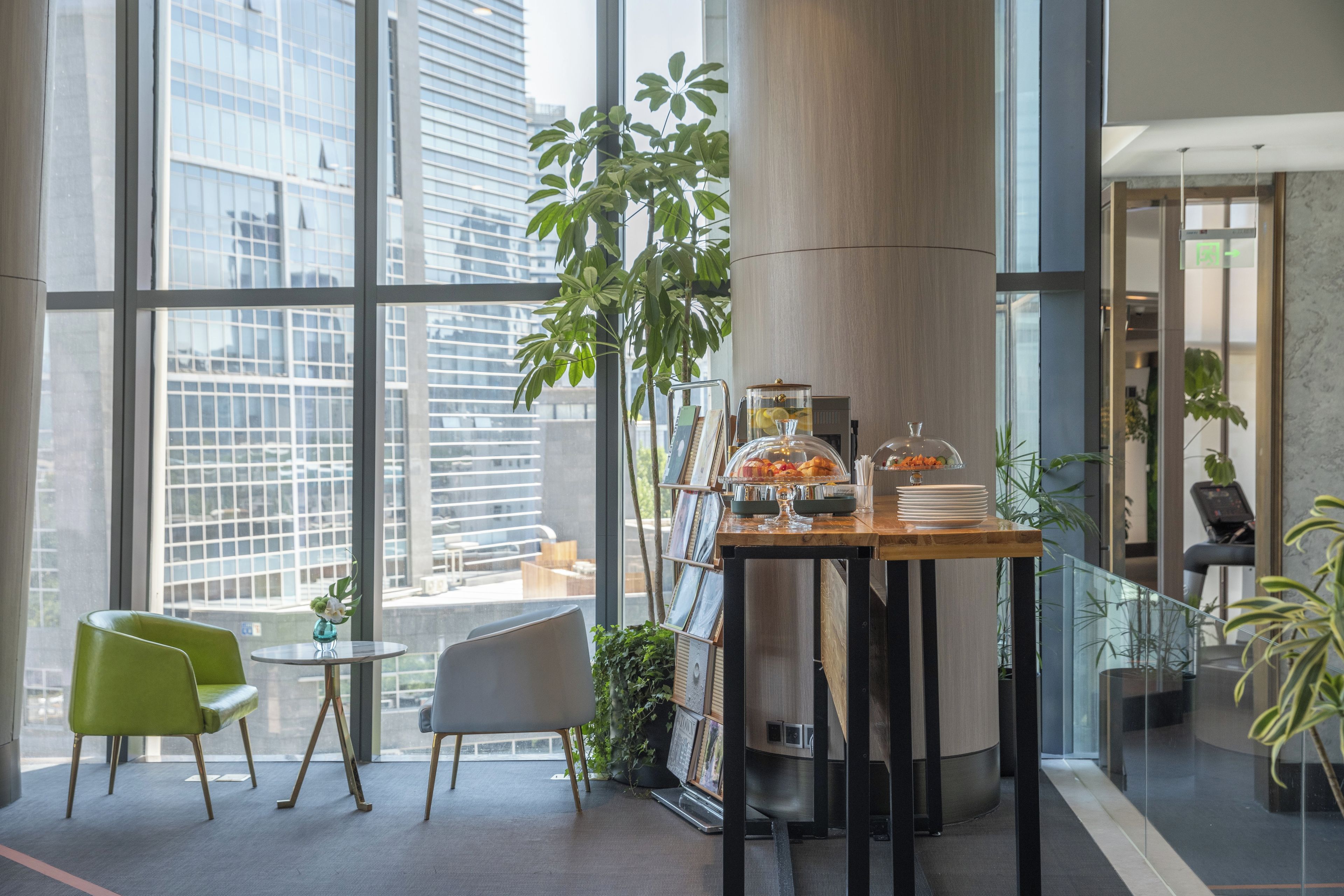 Een moderne ruimte met grote ramen, een houten tafel met een glazen koepel waarin eten is uitgestald, en groene stoelen.