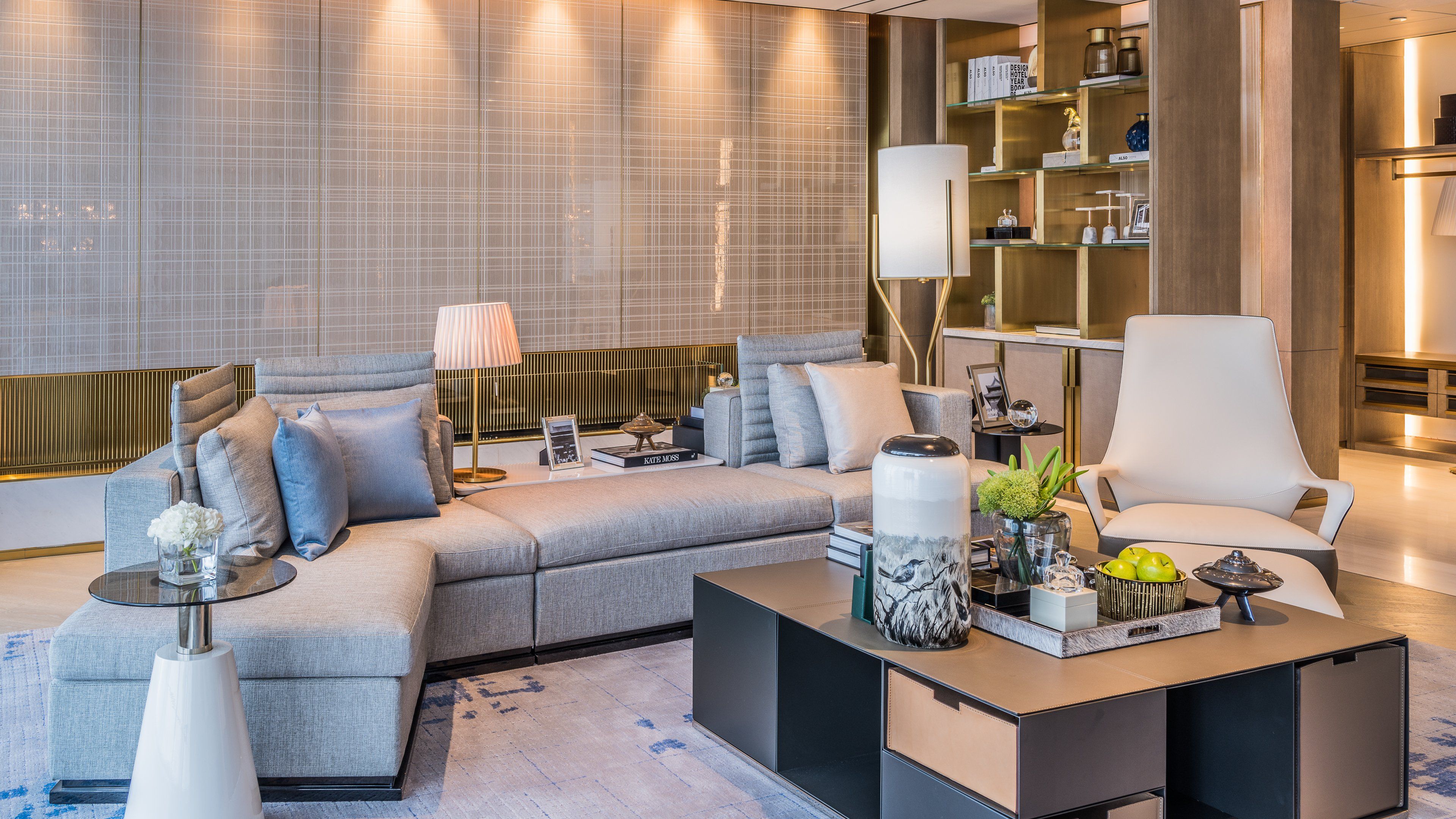 Un salon moderne comprenant un canapé d’angle, une table basse agrémentée d’objets décoratifs, une table d’appoint et une bibliothèque contenant des livres et d’autres objets décoratifs.