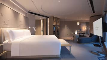 A modern hotel room with a large bed, a desk, a seating area, and a television.