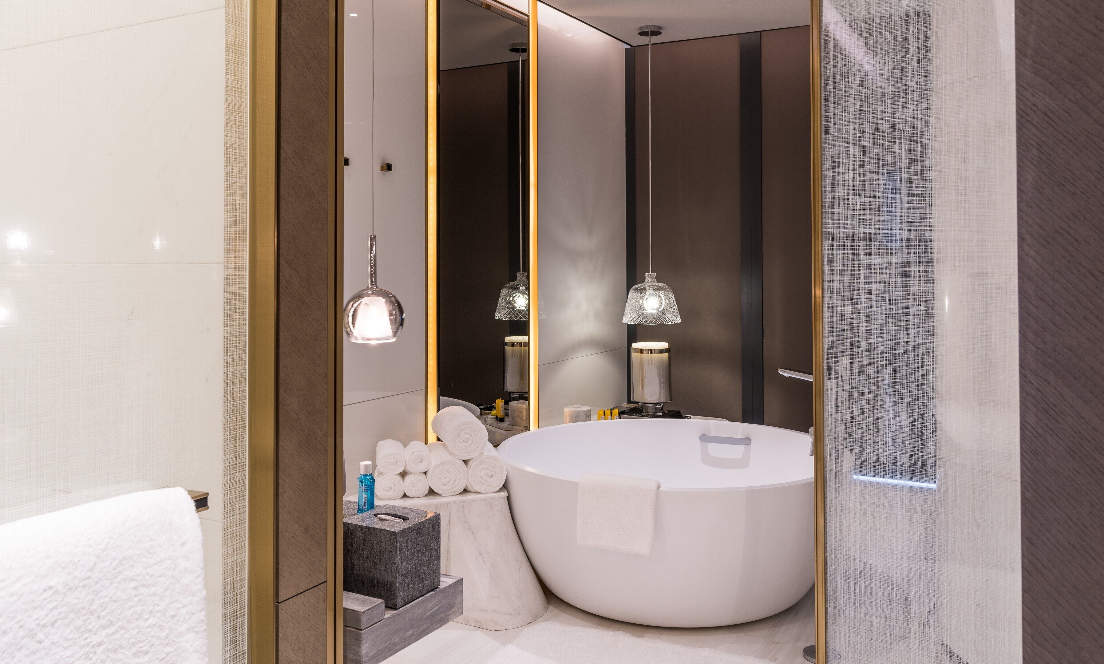 Un baño moderno con una bañera grande, un espejo redondo y dos lámparas colgantes.