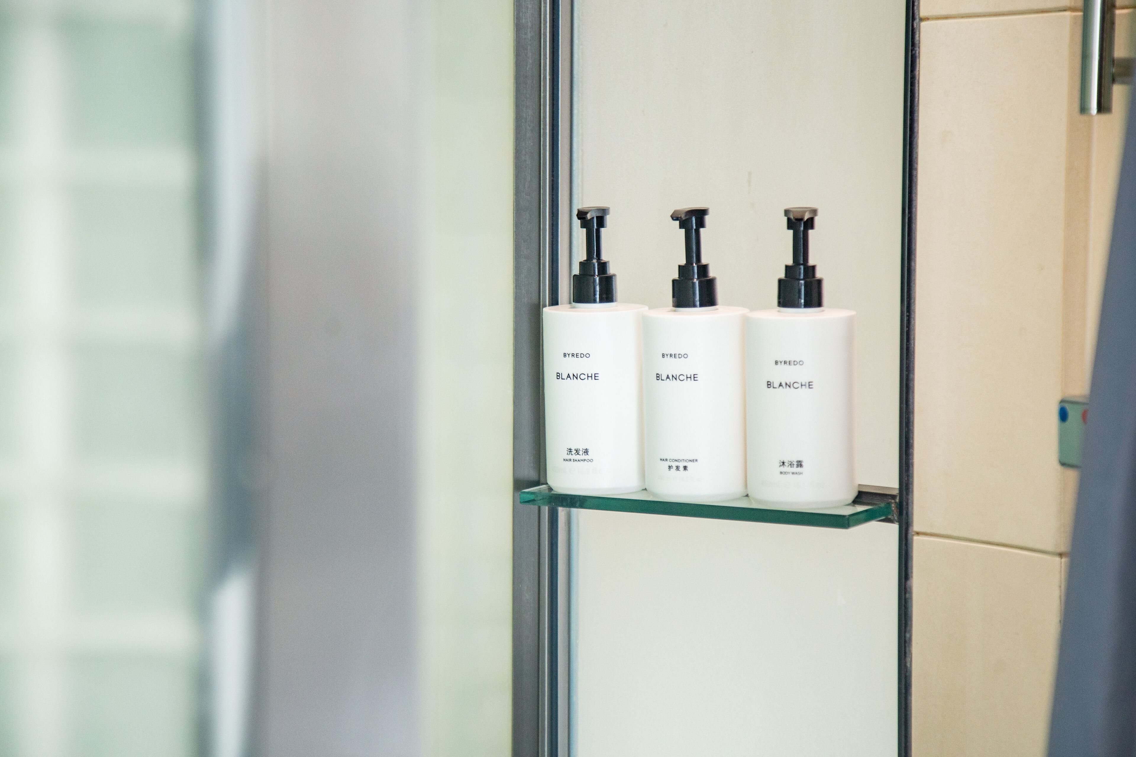 Three white bottles with black pumps on a glass shelf in a bathroom.