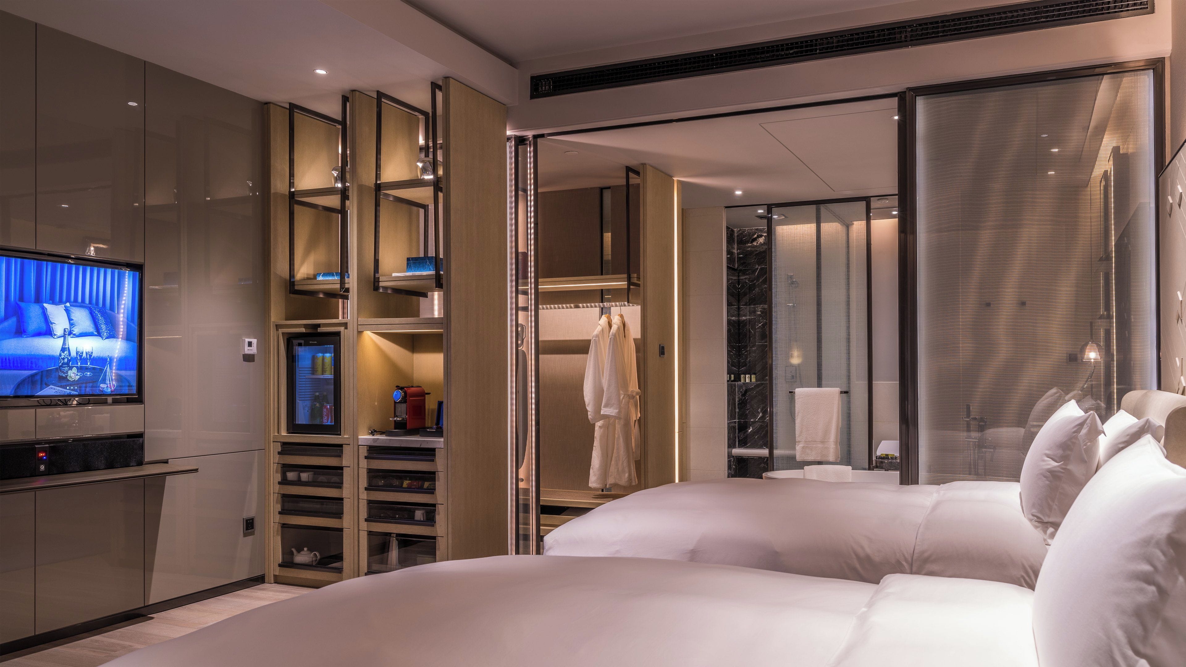 Una habitación de hotel moderna con una cama grande, televisión, minibar y vestidor.