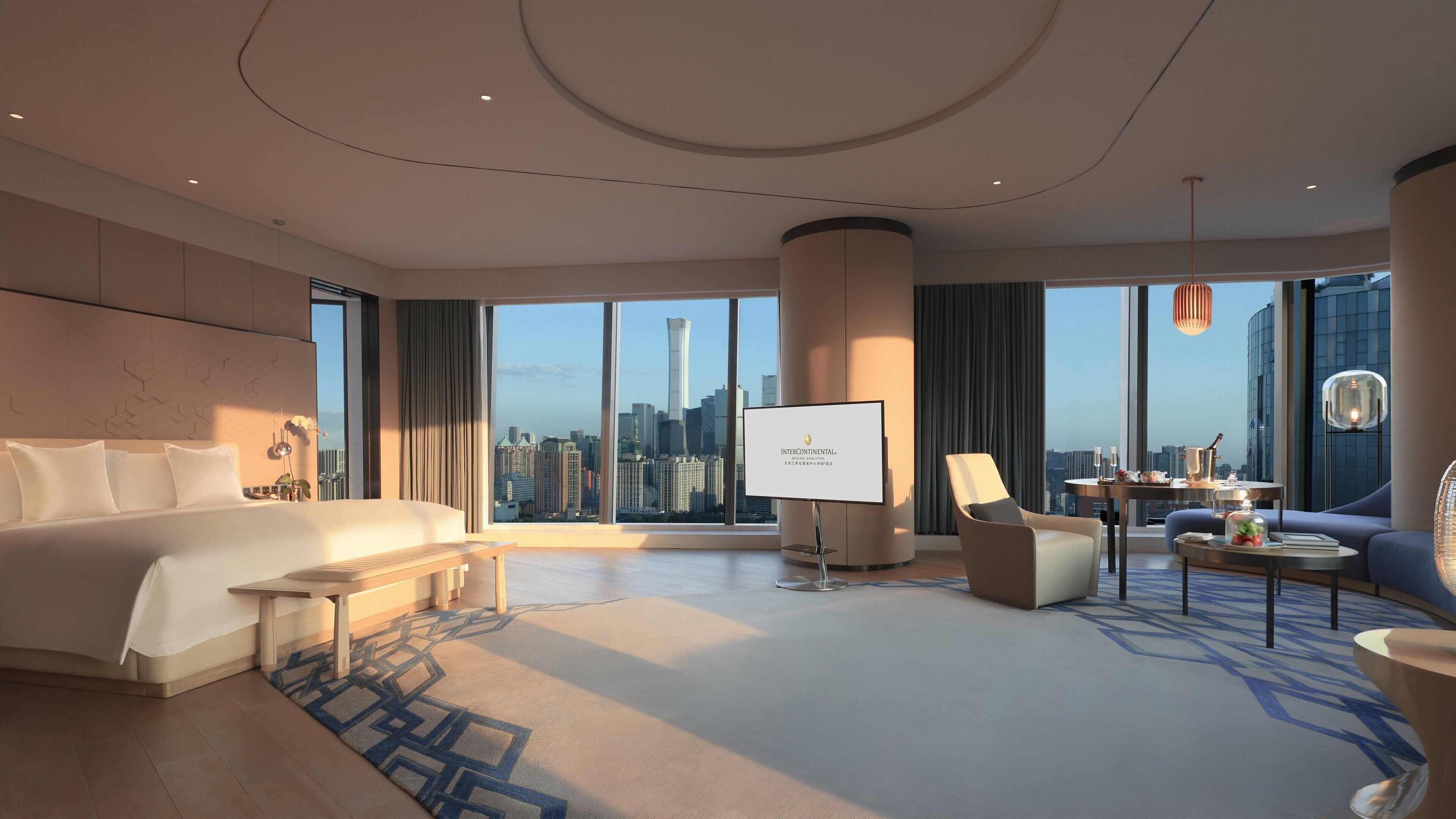 A spacious hotel room with a large bed, a seating area, a TV screen, and a city view.