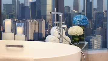 A modern bathroom with a large bathtub, a glass-enclosed shower, and a cityscape view.