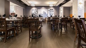 Un amplio comedor con mesas y sillas de madera, iluminación colgante moderna y una obra de arte grande en la pared.