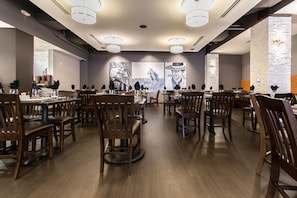 Un vaste espace dédié à la salle à manger, avec des tables et des chaises en bois, un éclairage moderne suspendu et de grandes œuvres d’art murales.