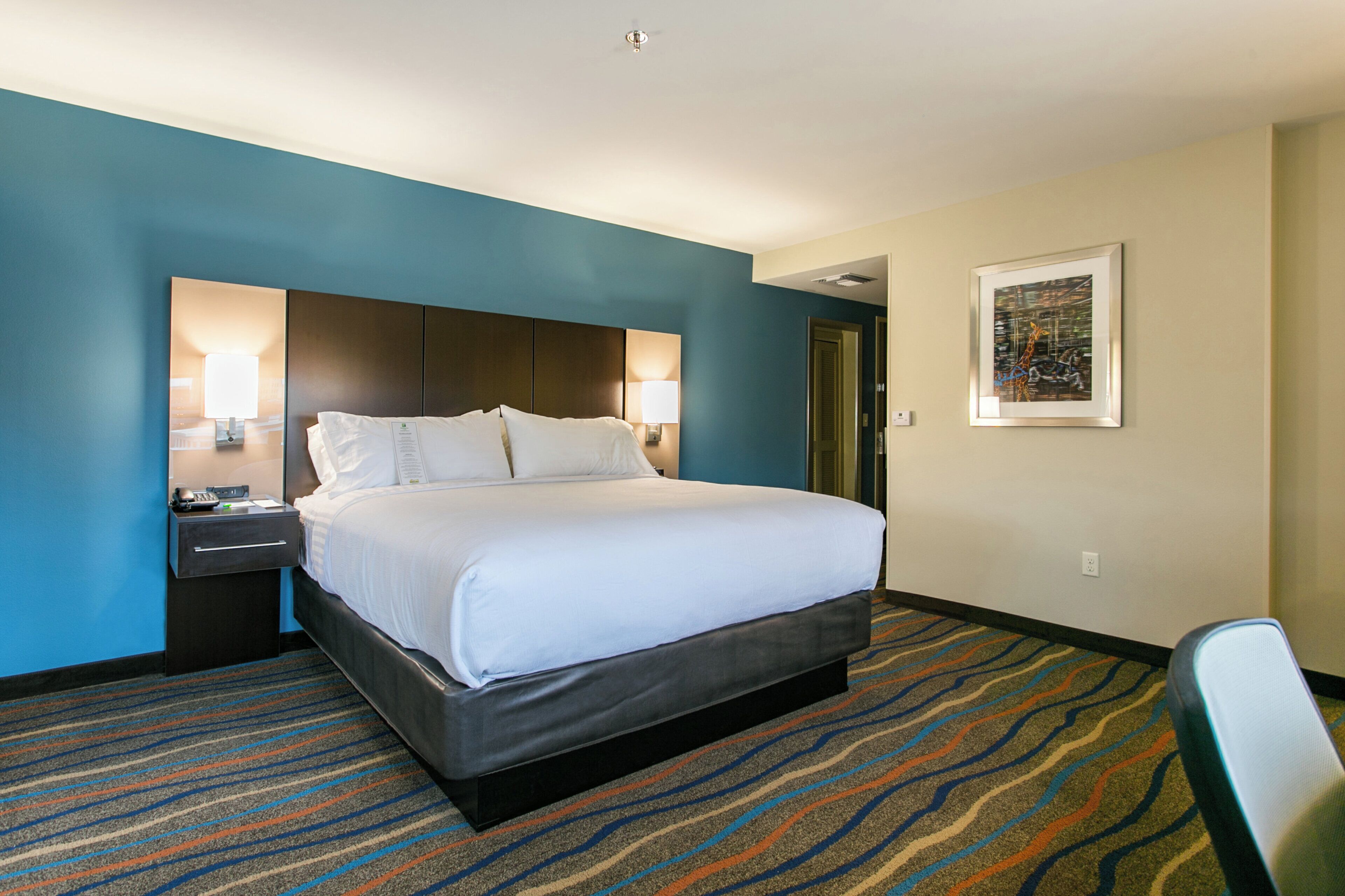 A hotel room with a large bed, a nightstand, a desk, and a chair.