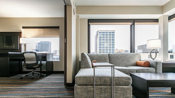 Habitación de hotel con vista a la ciudad, un escritorio con silla, un sofá y una pequeña mesa.