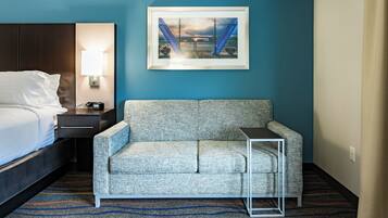 A hotel room with a bed, a sofa, a small table, a lamp, and a framed picture on the wall.