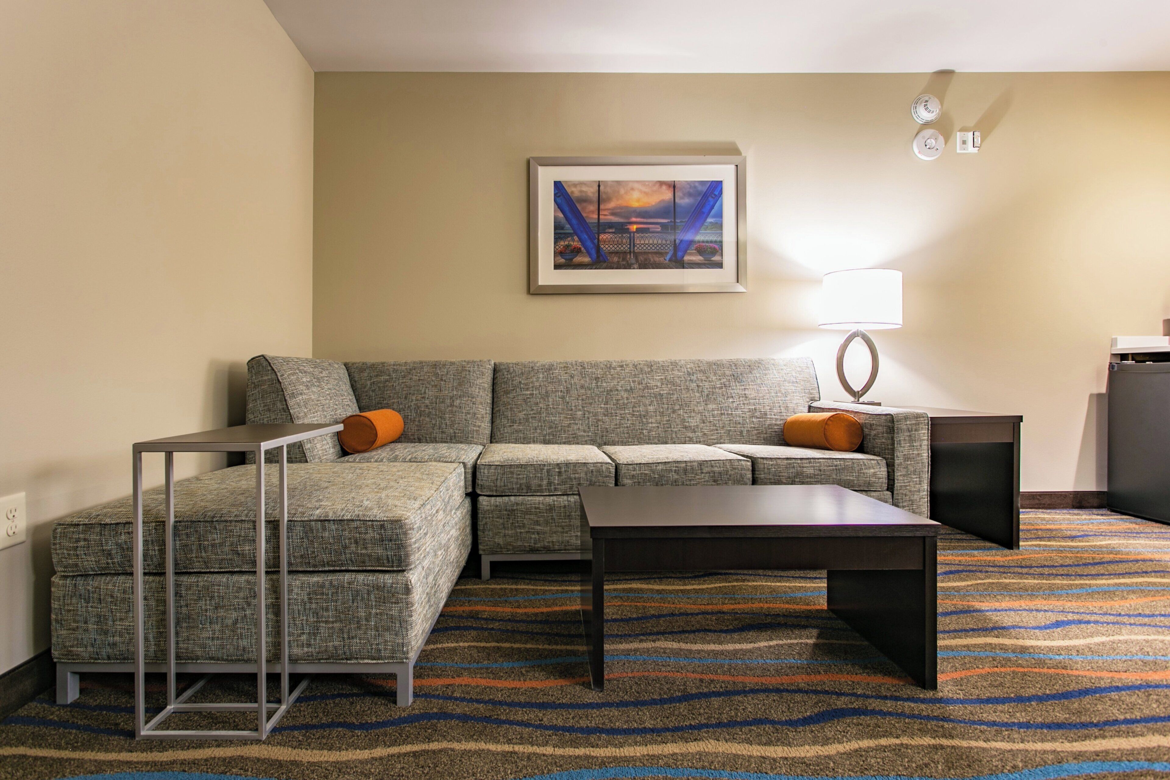 A living room with a sectional sofa, a coffee table, a lamp, and a painting on the wall.