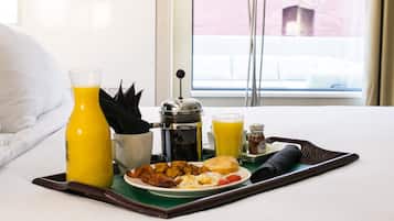 A breakfast tray with eggs, bacon, and toast, a coffee pot, and a bottle of orange juice on a hotel bed.