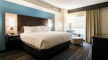 A hotel room with a large bed, a desk with a telephone, a chair, and a desk lamp.