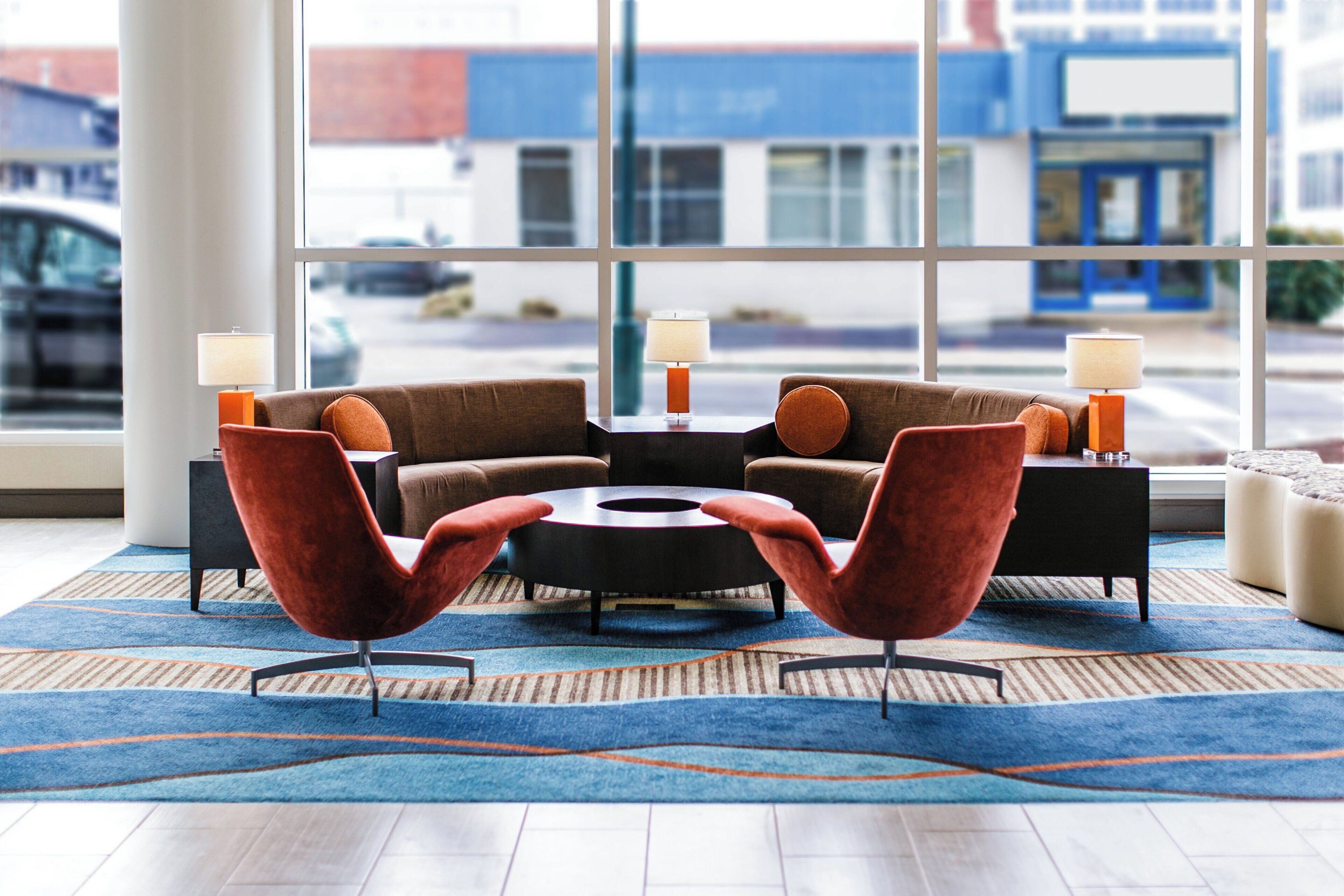 A modern hotel lobby with a sectional sofa, two armchairs, a coffee table, and a rug.