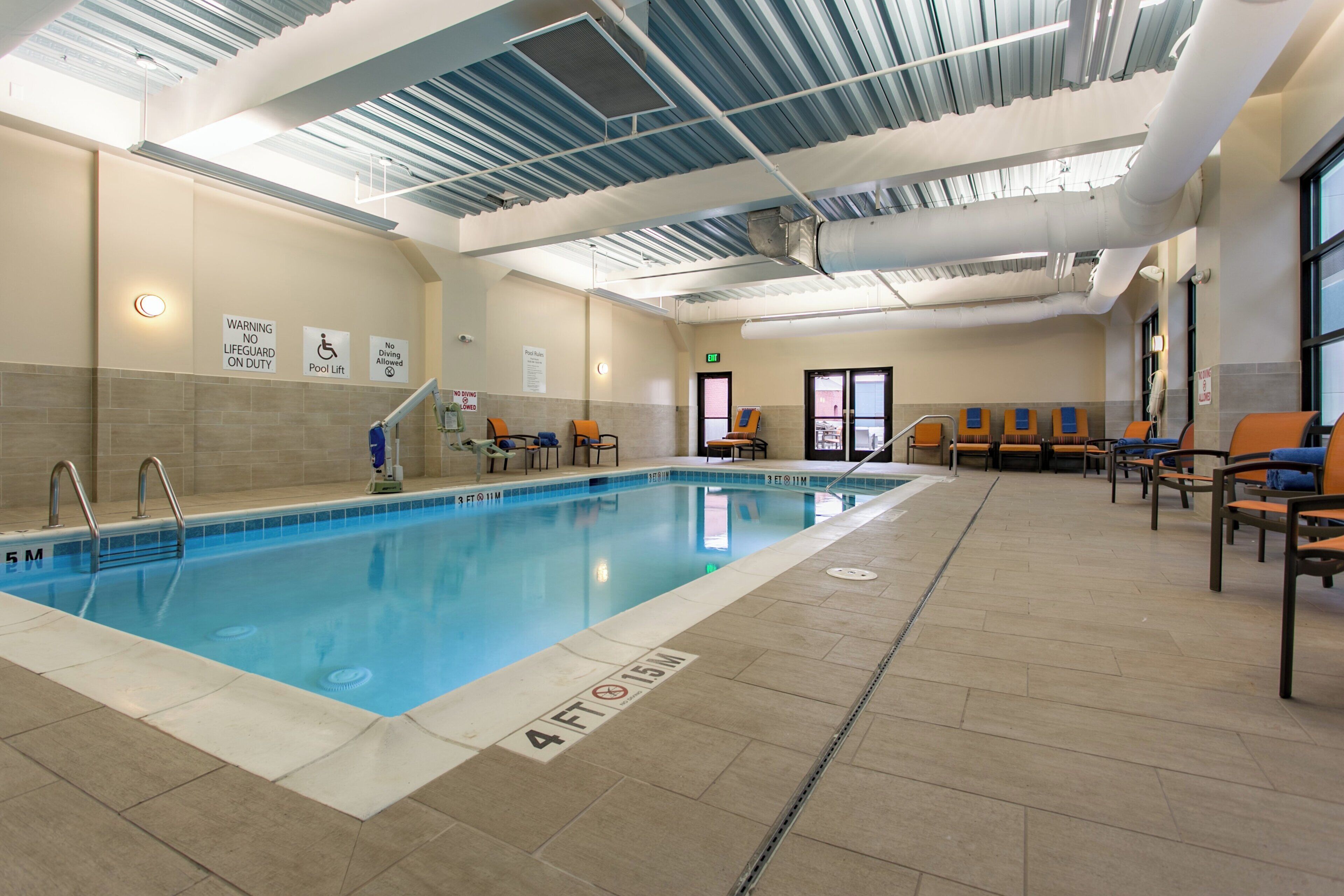 Ein Hallenbad mit gut sichtbaren Wassertiefenmarkierungen, einer Rettungsschwimmerstation und einem Lifter für das Schwimmbecken.