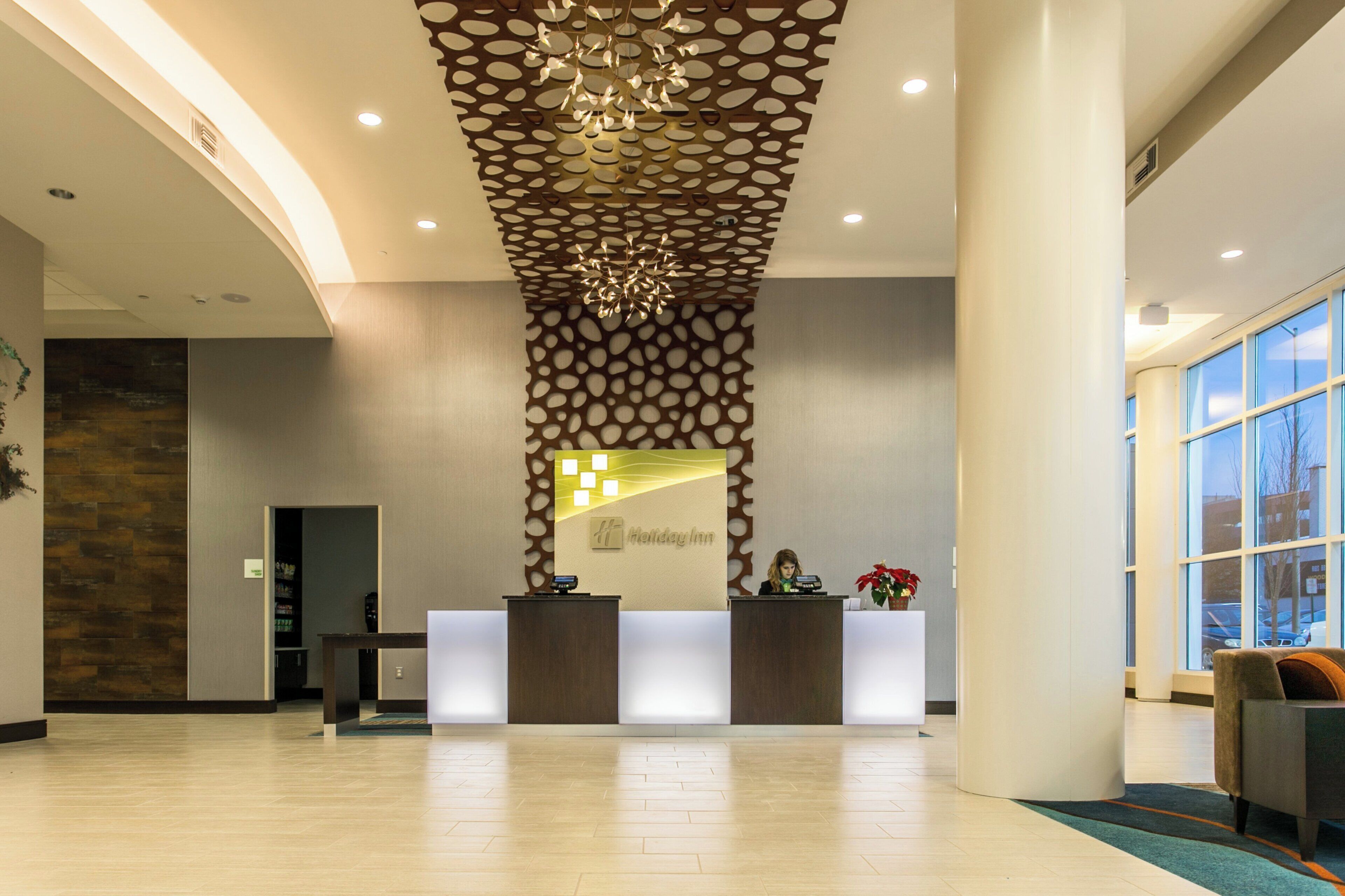 A hotel reception area with a modern design, featuring a reception desk, a decorative ceiling, and a large window providing a view outside.
