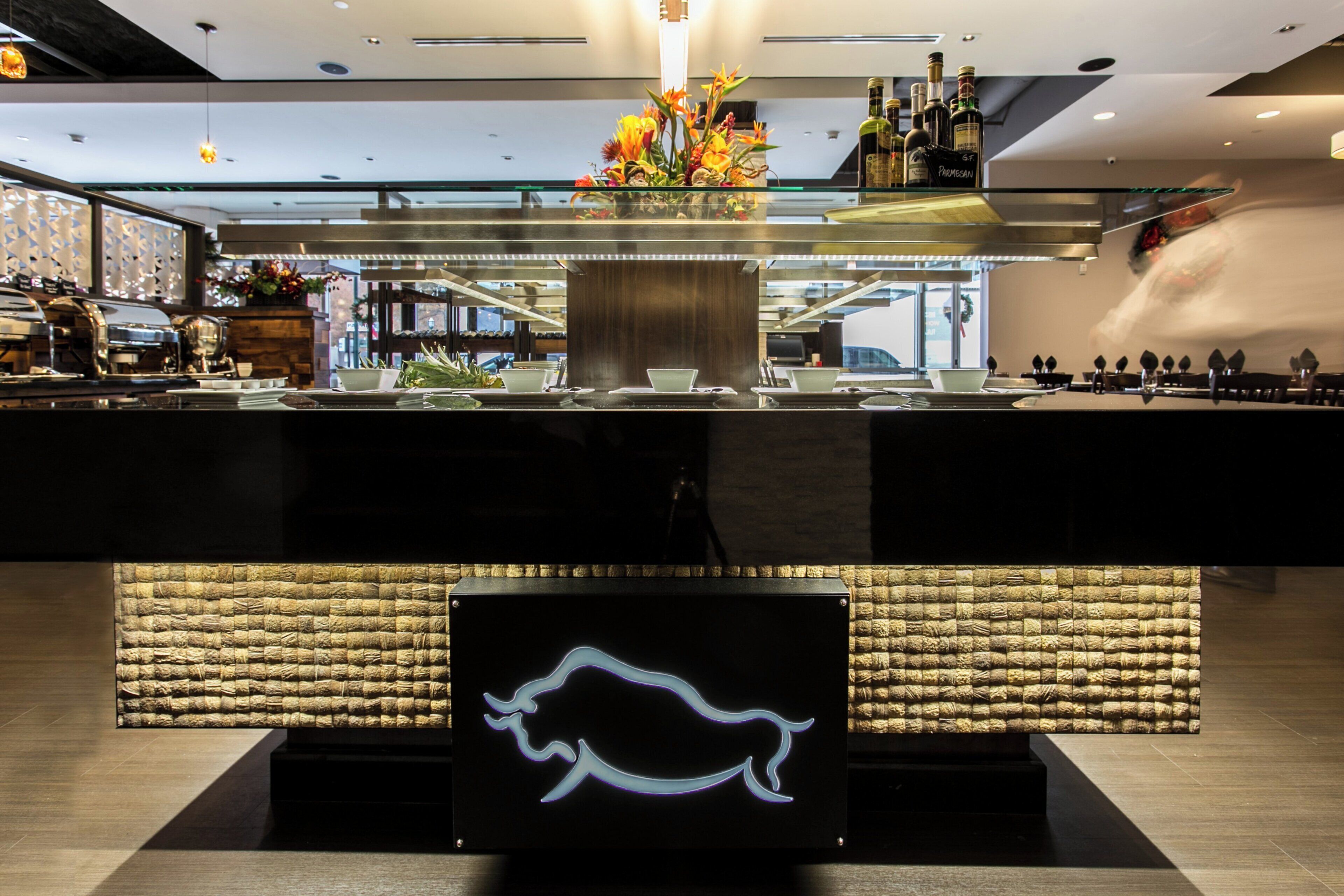 A modern bar area with a glass partition, a neon pig sign, and various bottles.