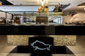 A modern bar area with a glass partition, a neon pig sign, and various bottles.
