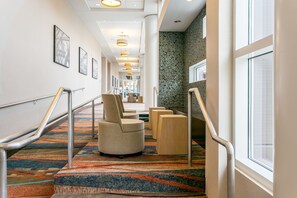 A hotel corridor with a patterned carpet, metal handrails, and framed pictures on the walls.
