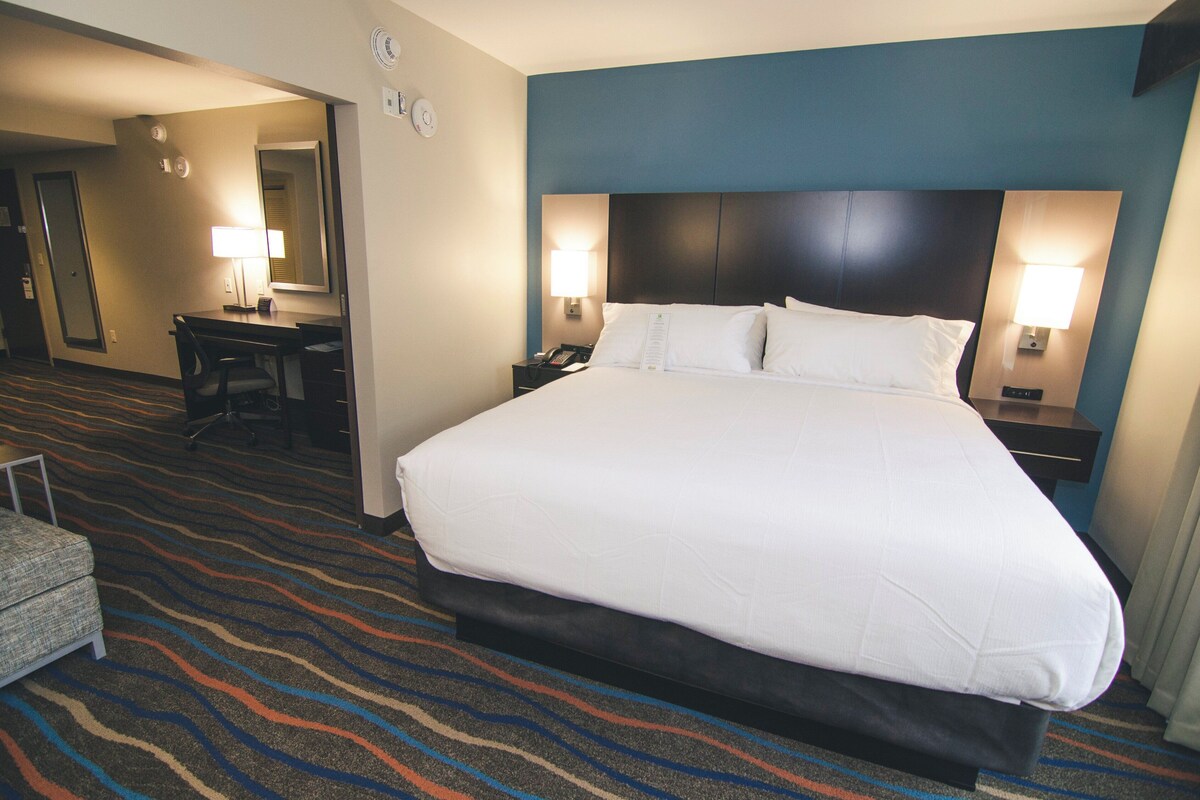 A hotel room with a large bed, a desk, and two bedside lamps.