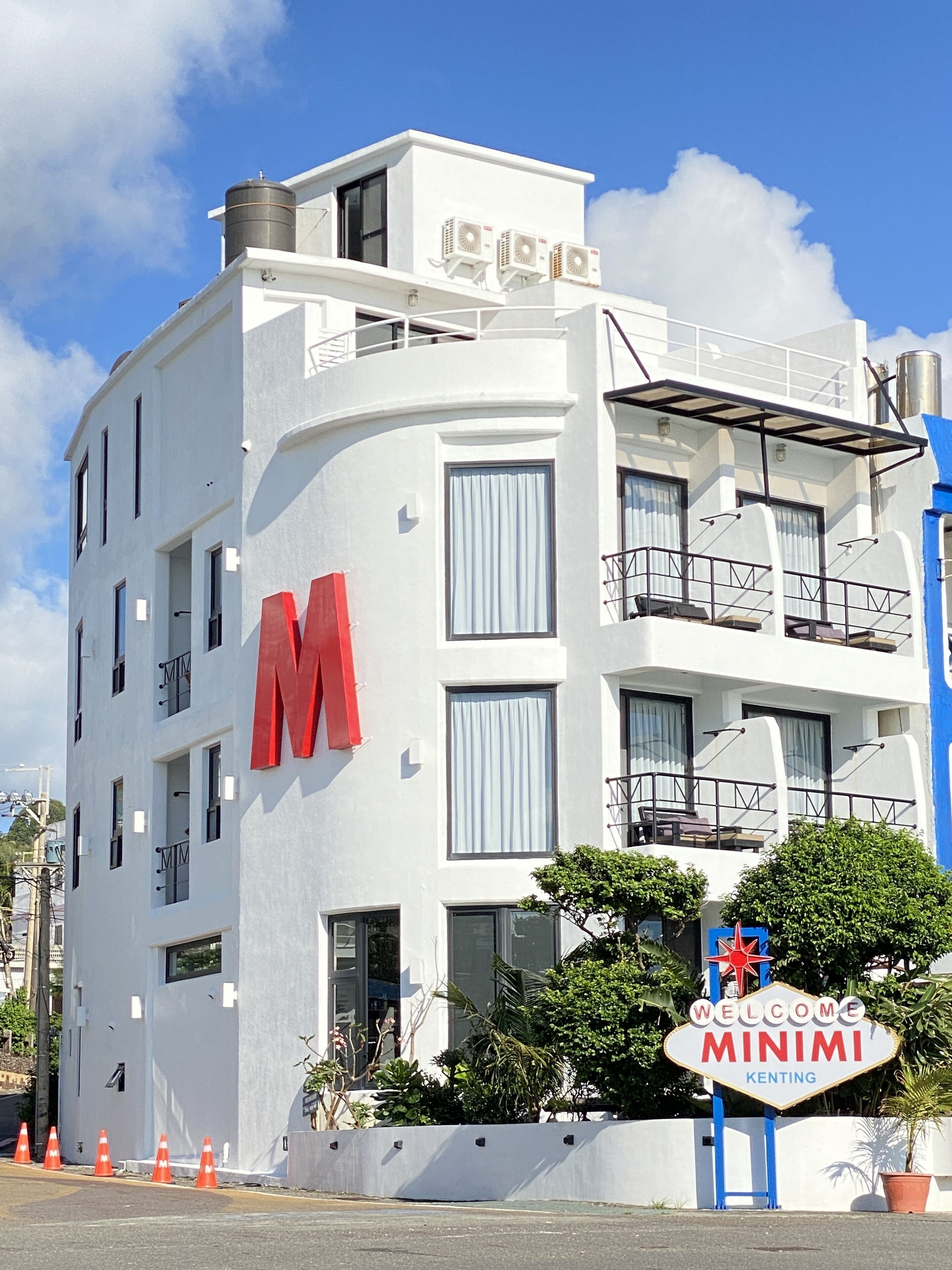 Un bâtiment blanc avec un grand « M » rouge sur le côté, une enseigne indiquant « Bienvenue chez Mini » et des balcons dotés de garde-corps.