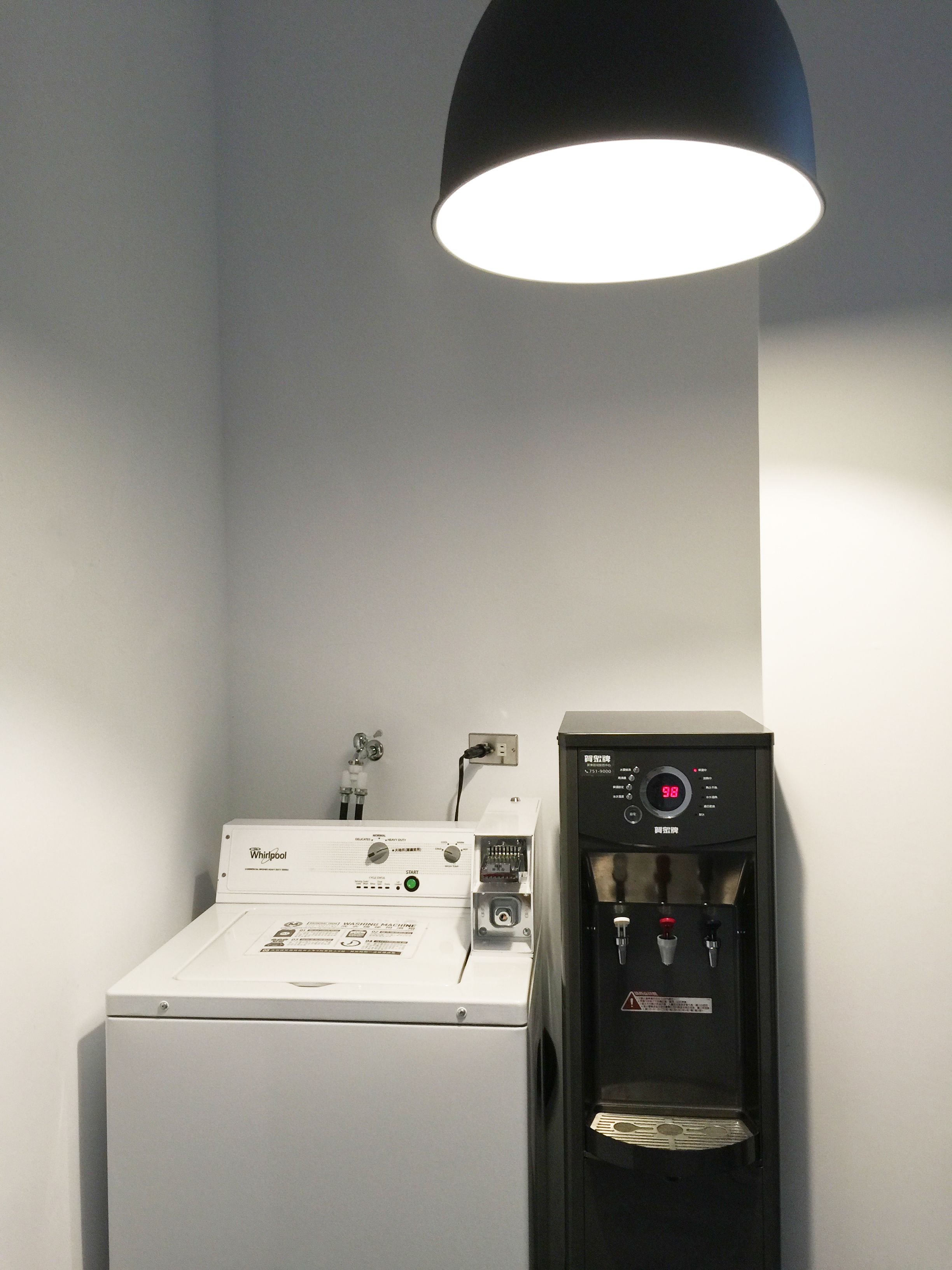 Une petite buanderie équipée d’une machine à laver Whirlpool et d’un distributeur d’eau.