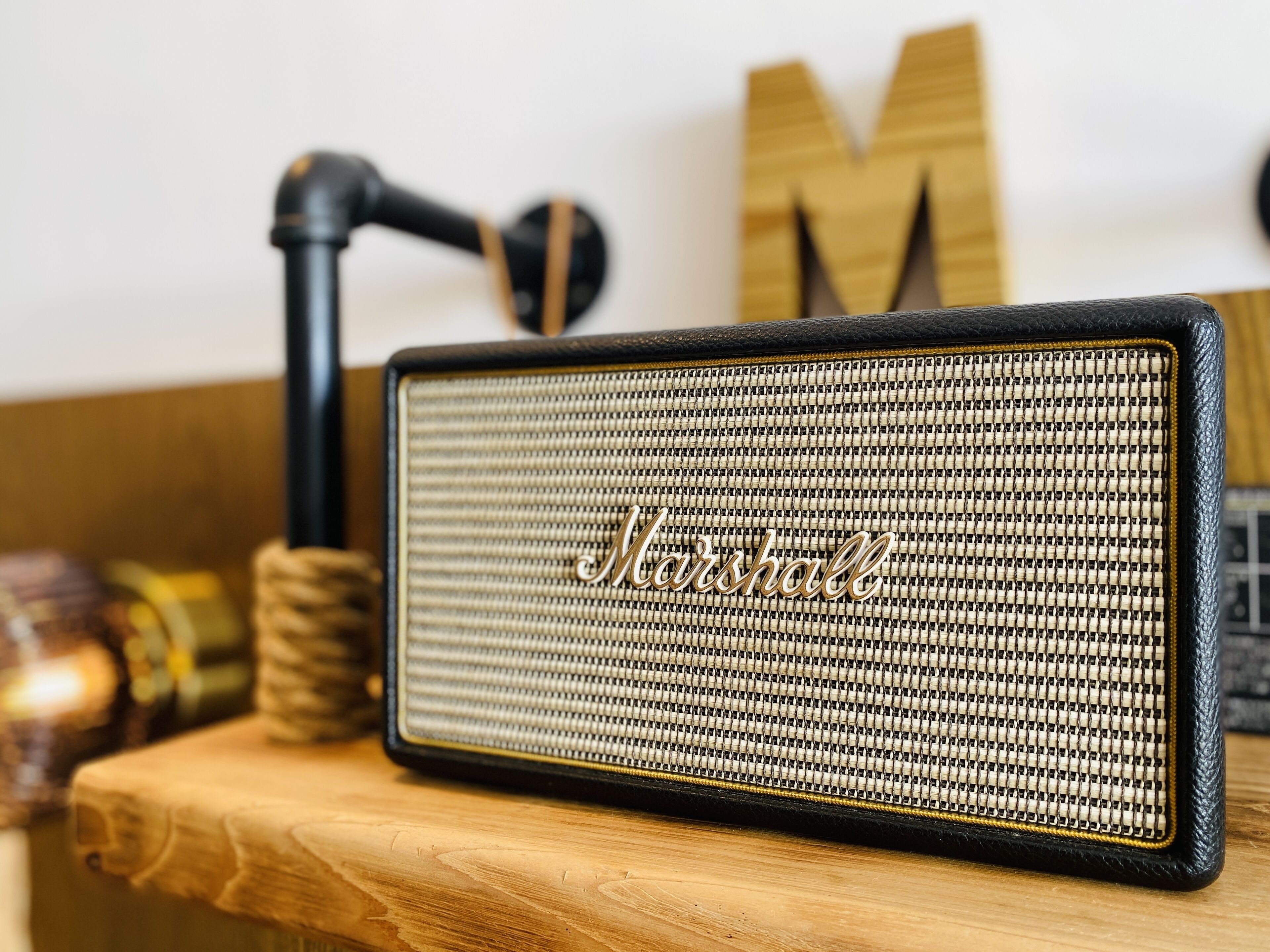 A Marshall speaker on a wooden surface with a microphone stand and a wooden 'M' letter in the background.