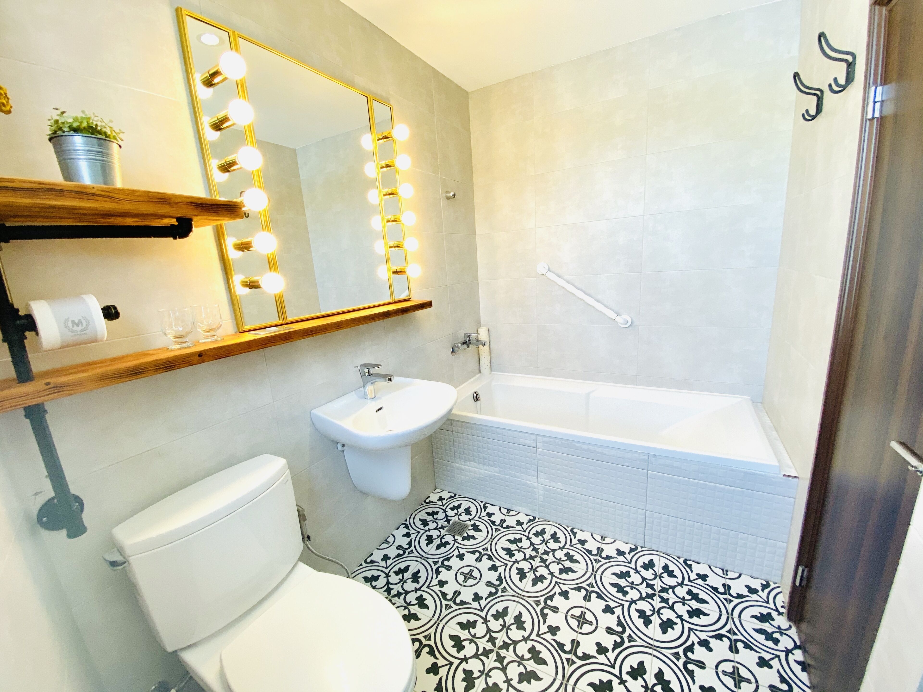 A bathroom with a toilet, sink, and bathtub. There is a mirror with lights above it, and a towel rack.