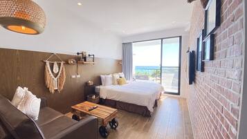 A modern hotel room with a large bed, a sofa, a wooden coffee table, and a view of the ocean.