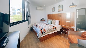 A modern bedroom with a large bed, a TV, a desk, and a chair.