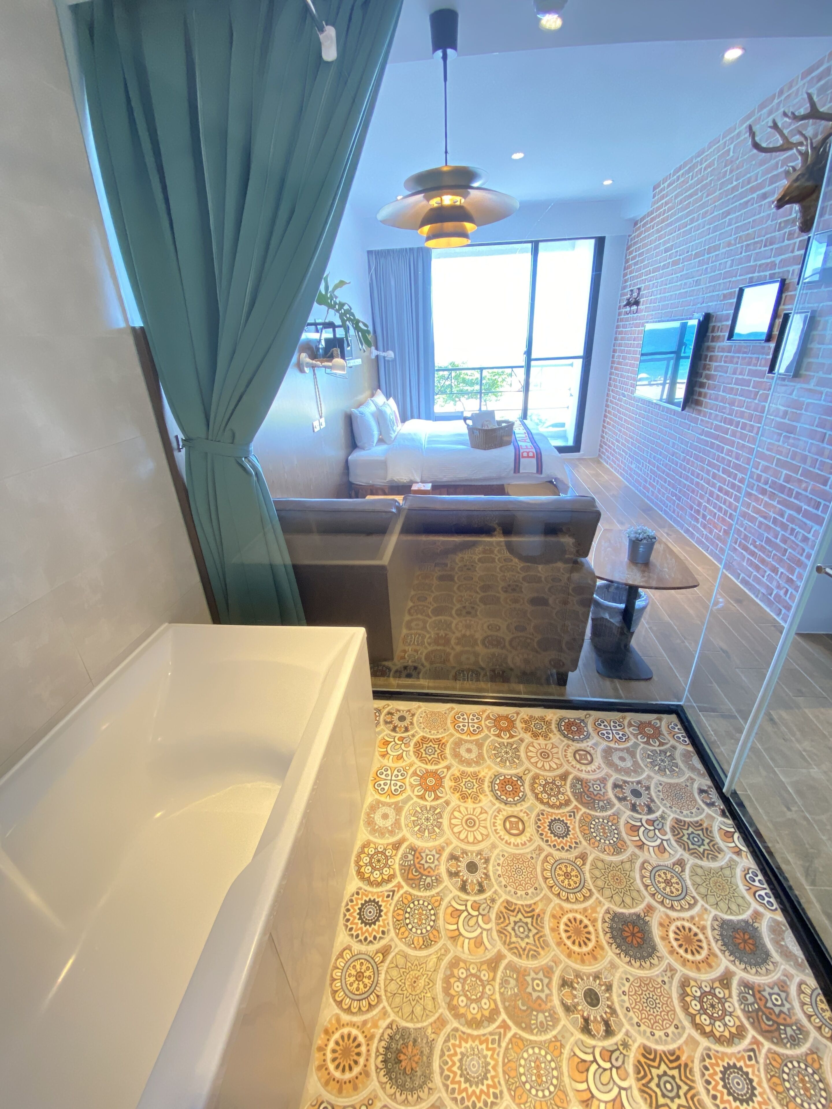 A modern bathroom with a bathtub, patterned floor tiles, a sofa, and a large window providing natural light.