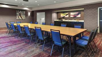 Un salón de conferencias con una mesa larga, sillas azules, una zona de cocina y una puerta.