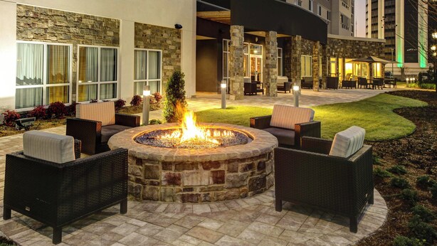 A stone fire pit surrounded by wicker furniture in an outdoor patio area of a hotel. - Courtyard by Marriott New Orleans Westbank/Gretna (Gretna)
