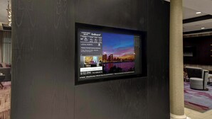 A digital display in a lobby with a cityscape background, a weather widget, and a local event notification. - Courtyard by Marriott New Orleans Westbank/Gretna (Gretna)