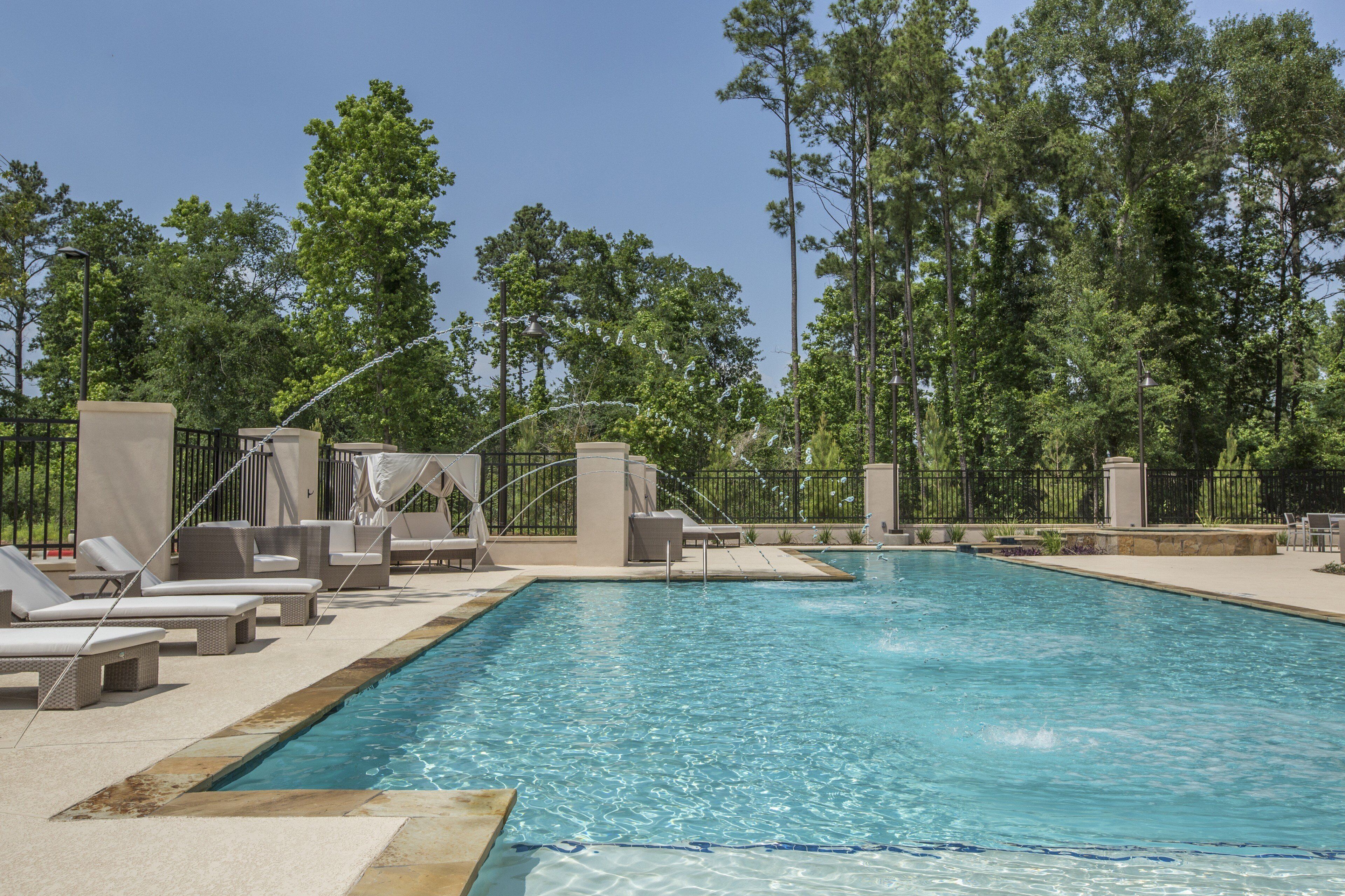 A swimming pool with lounge chairs and umbrellas, surrounded by a fence and trees.