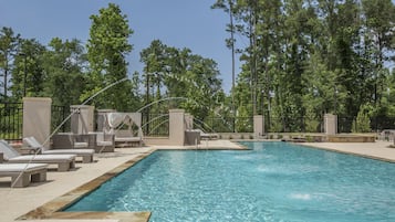 A swimming pool with lounge chairs and umbrellas, surrounded by a fence and trees.